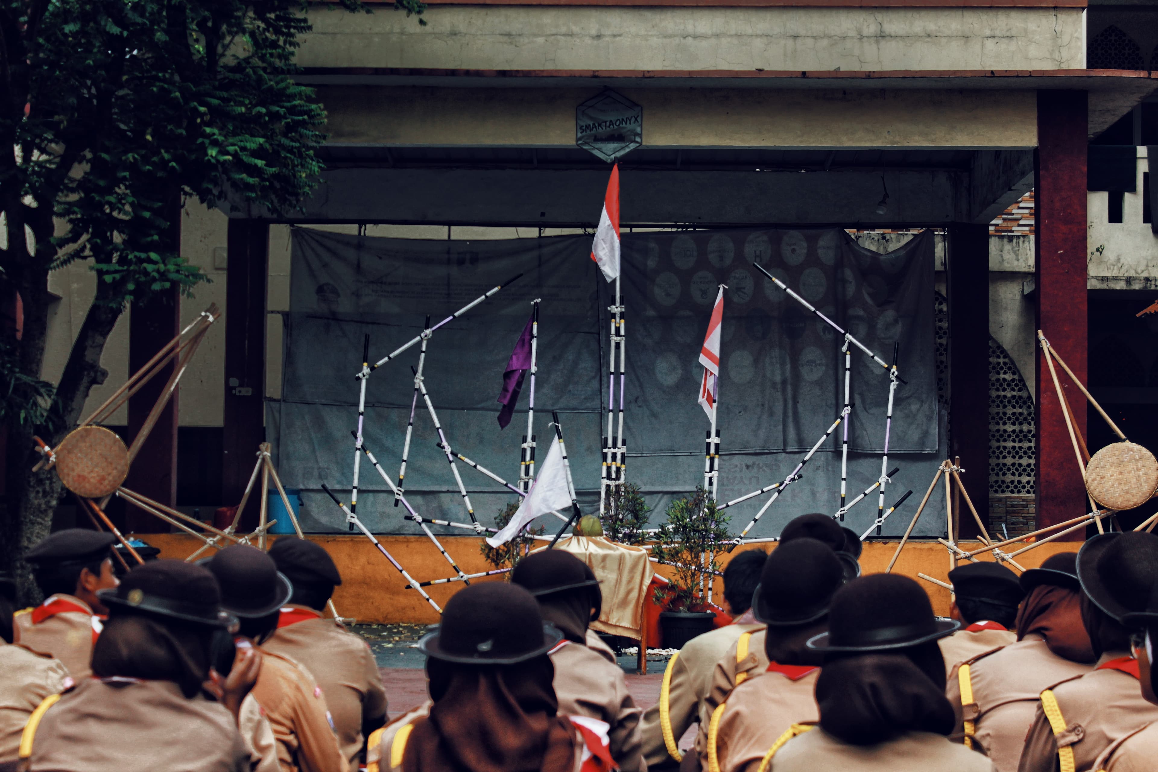 Anggota pramuka duduk menghadap panggung yang menampilkan struktur pionering kayu dan bendera merah putih.