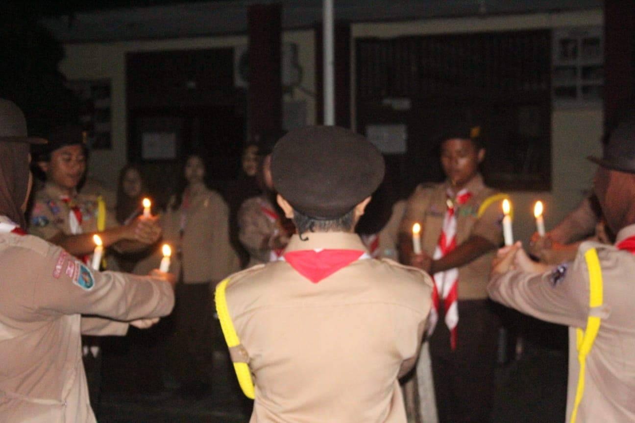 Anggota pramuka memegang lilin menyala dalam formasi lingkaran saat upacara di malam hari.