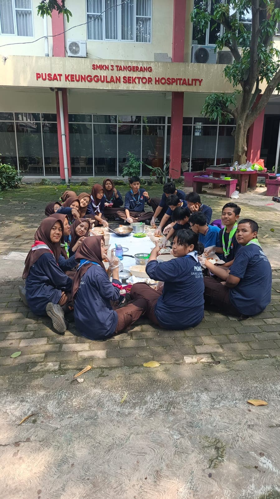 Sekelompok siswa Pramuka makan bersama secara lesehan di halaman depan gedung SMKN 3 Tangerang.