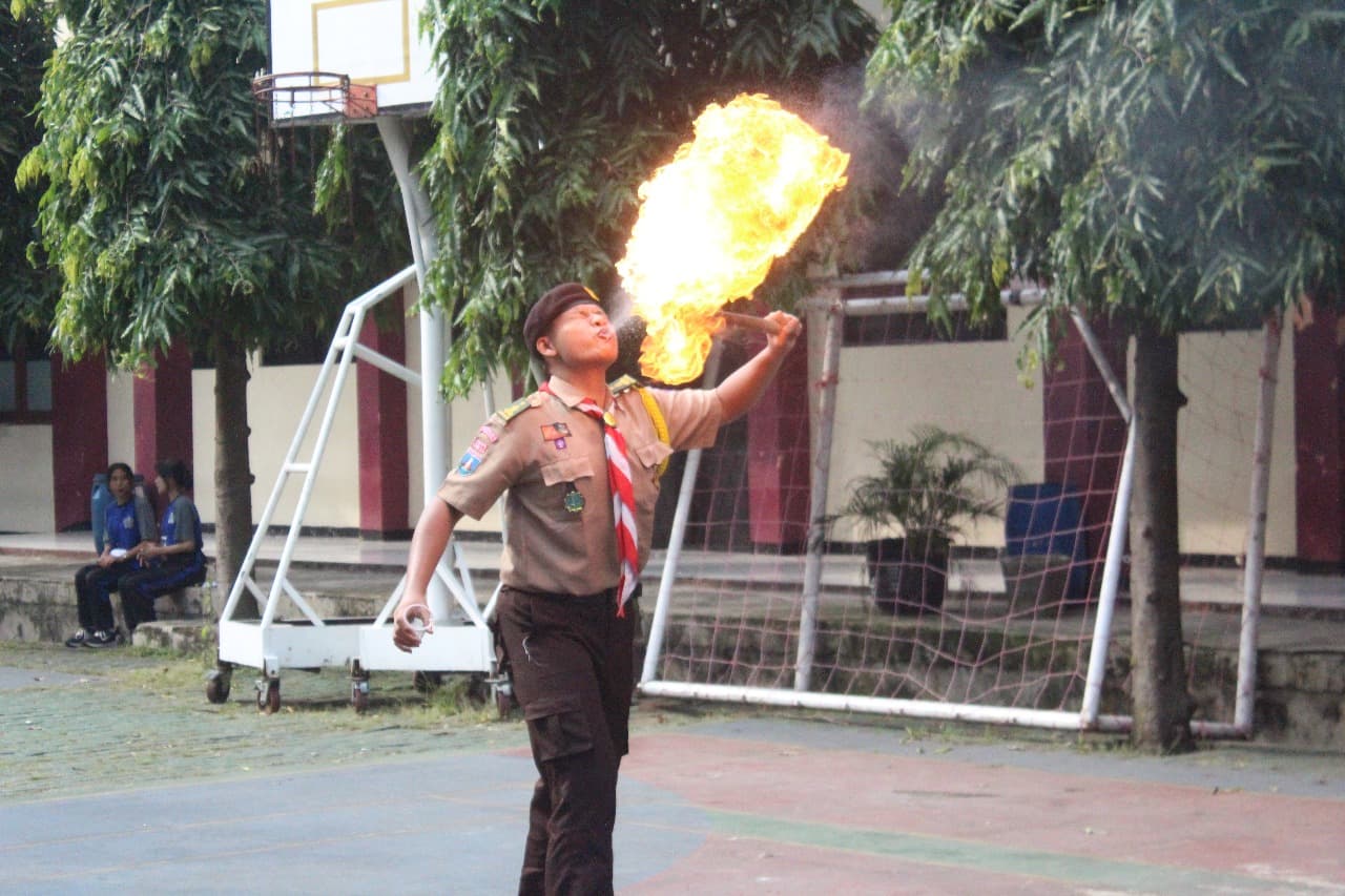 Anggota Pramuka melakukan atraksi sembur api yang menghasilkan bola api besar di lapangan sekolah.
