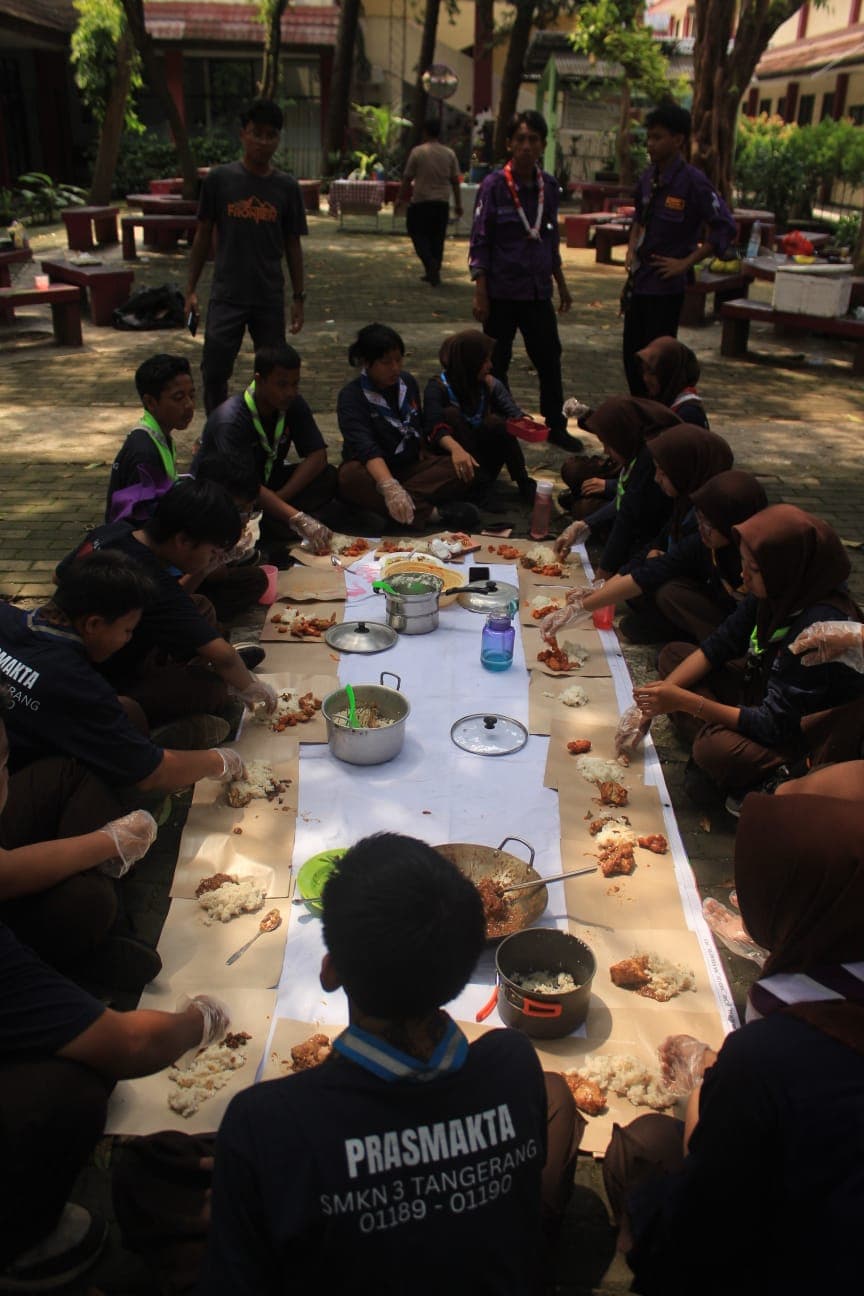 Siswa PRASMAKTA makan bersama beralaskan kertas di halaman sekolah dalam suasana penuh kebersamaan yang akrab.