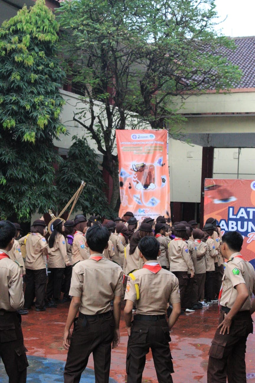 Sekelompok anggota pramuka berseragam cokelat berkumpul di lapangan sekolah untuk mengikuti kegiatan latihan gabungan.