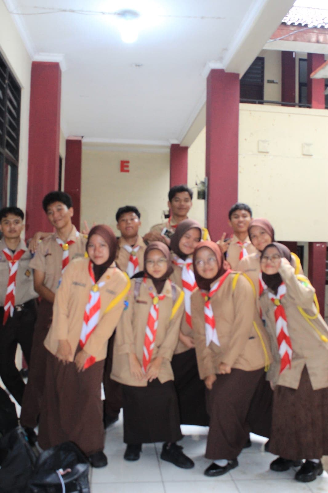 Sekelompok siswa Indonesia mengenakan seragam pramuka cokelat dan hasduk merah putih di lorong sekolah.