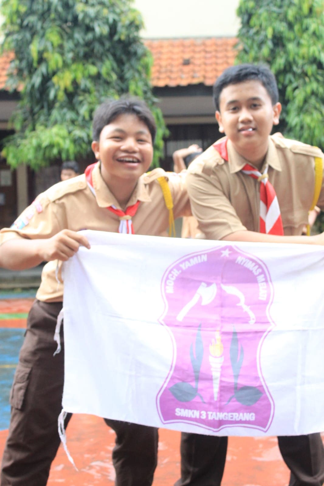 Dua siswa berseragam pramuka tersenyum lebar sambil memegang bendera putih berlogo SMKN 3 Tangerang.