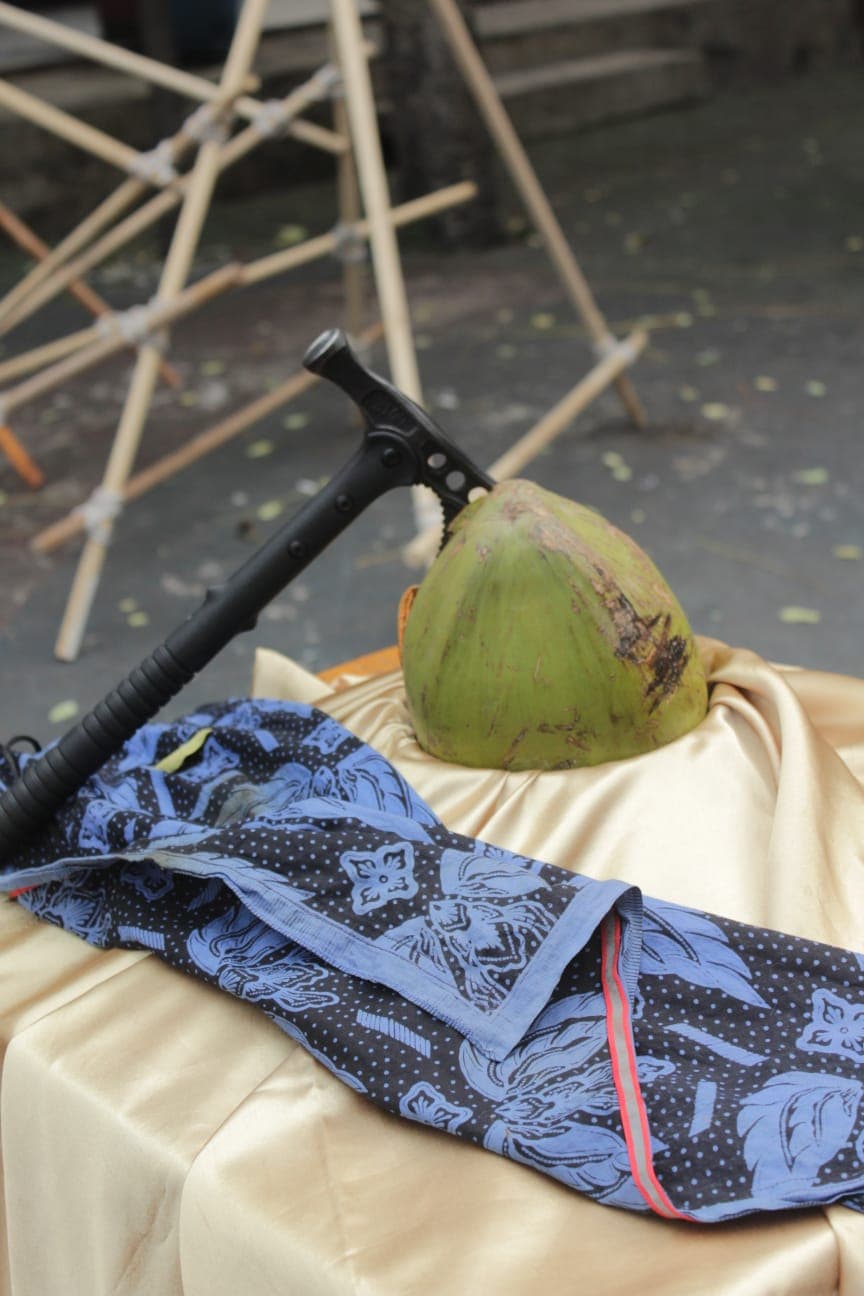 Kapak hitam menancap di kelapa hijau di atas kain satin emas dan kain batik biru.